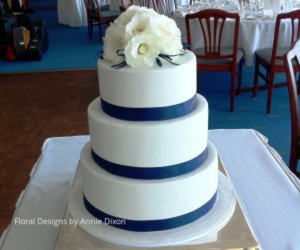 3 tier round wedding cake decorated with white Lisianthus and navy ribbon