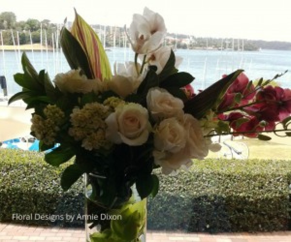 A glass cylinder arrangement of Cymbidiums, Roses and Hydrangea in bay window